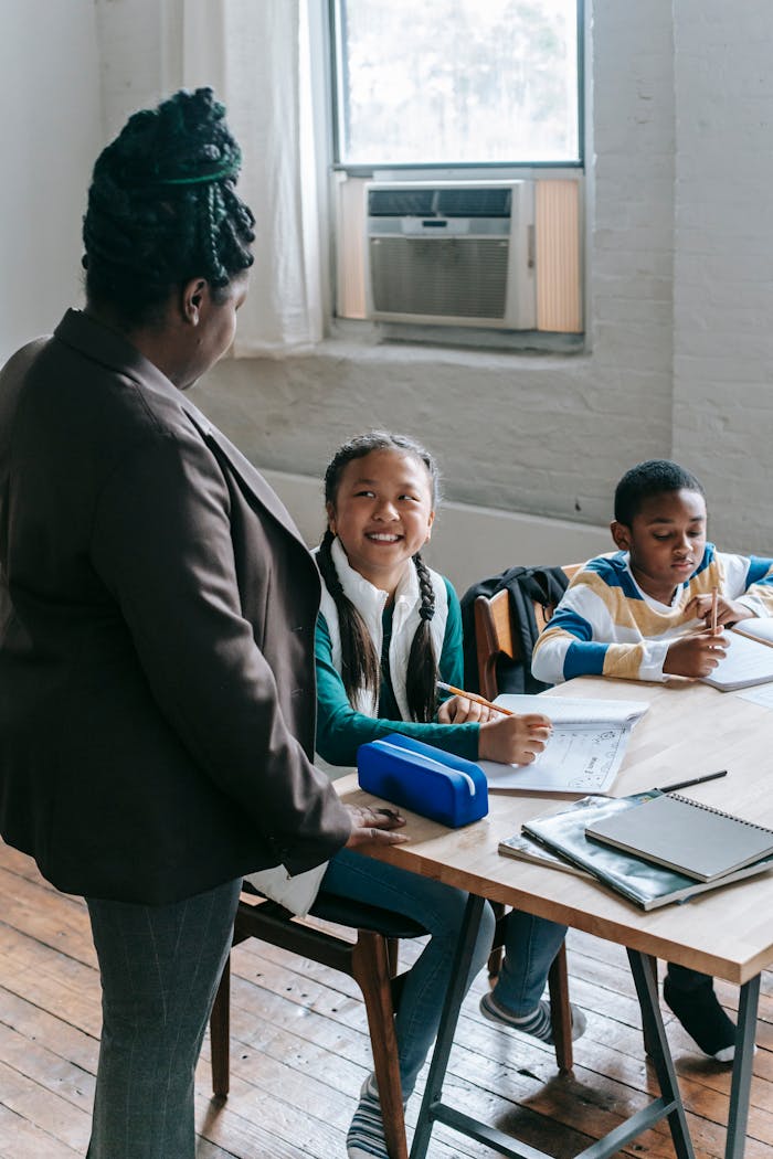 African American female teacher standing near school bench and talking to smiling multiracial classmates